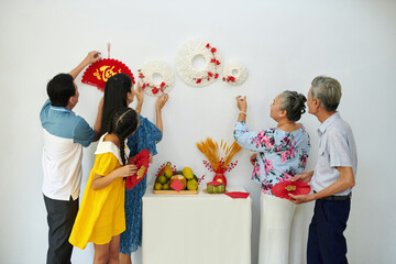 Family hanging traditional Tet decorations on wall when preparing for Spring festival