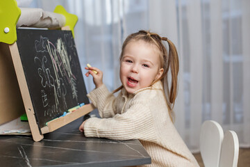 Fototapeta na wymiar Early brain development. Toddler girl draws on blackboard at home. Smiling
