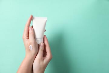 Woman with tube of hand cream on turquoise background, closeup. Space for text