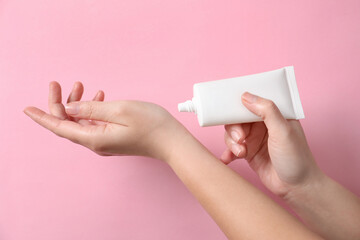 Woman applying cosmetic cream from tube onto her hand on pink background, closeup
