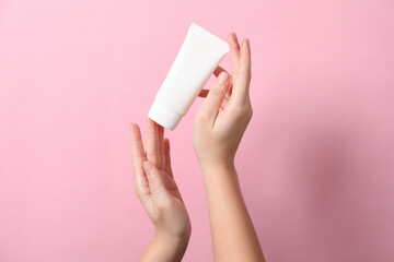 Woman with tube of hand cream on pink background, closeup