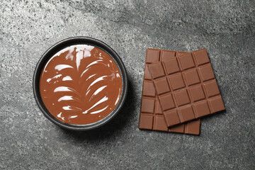 Tasty milk chocolate paste in bowl and bars on gray table, top view