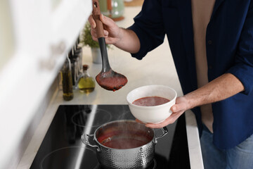 Man pouring delicious tomato soup into bowl in kitchen, closeup