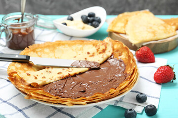 Tasty crepes with chocolate paste and berries served on turquoise wooden table, closeup