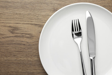 Plate, fork and knife on wooden table, top view. Space for text