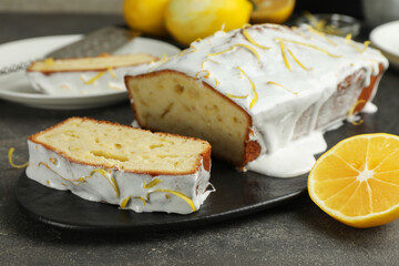Tasty lemon cake with glaze and citrus fruit on table, closeup