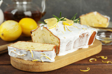 Tasty lemon cake with glaze and citrus fruits on wooden table, closeup