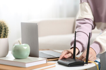 Woman connecting cable to Wi-Fi router at table indoors, closeup