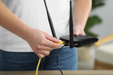 Woman inserting ethernet cable into Wi-Fi router at table indoors, closeup