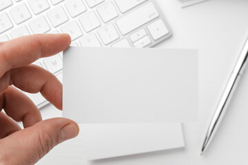 Woman with blank business card at white table, closeup. Mockup for design