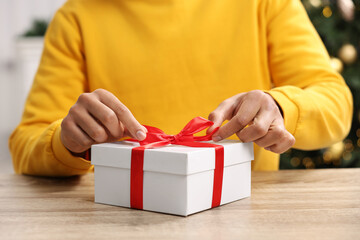 Man opening Christmas gift at wooden table indoors, closeup