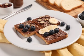 Fototapeta na wymiar Toasts with tasty nut butter, banana slices, blueberries and hazelnuts on table, closeup