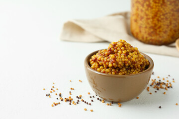Fresh whole grain mustard in bowl and dry seeds on white table. Space for text