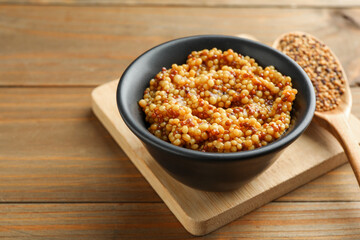 Fresh whole grain mustard in bowl on wooden table. Space for text