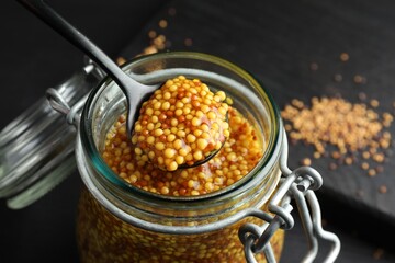 Taking whole grain mustard with spoon from jar on table, closeup