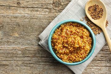 Fresh whole grain mustard in bowl and dry seeds on wooden table, flat lay. Space for text
