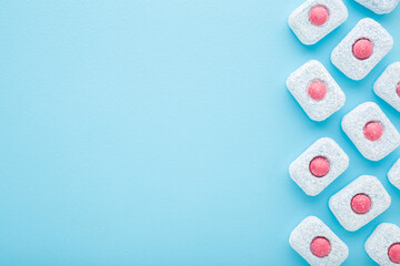 Row of red white blue dishwasher tablets on light blue table background. Pastel color. Closeup. Empty place for text. Top down view.