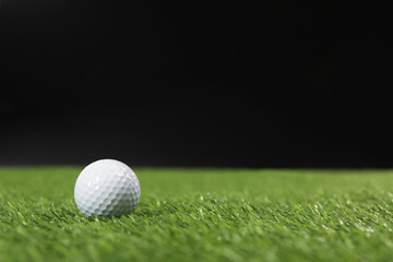 Golf ball on green grass against black background, space for text