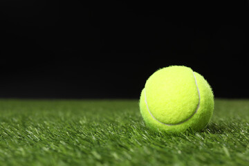 Tennis ball on green grass against black background, space for text