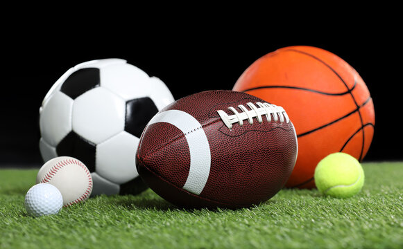 Many different sports balls on green grass against black background © New Africa