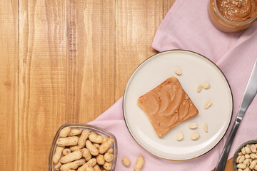 Toast with tasty nut butter and peanuts on wooden table, flat lay. Space for text