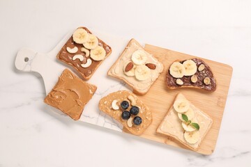 Toasts with different nut butters, fruits and nuts on white marble table, flat lay
