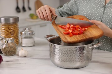 Cooking process. Woman adding cut bell pepper into pot at white marble table in kitchen, closeup