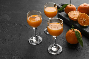 Tasty tangerine liqueur in glasses and fresh citrus fruits on black textured table. Space for text