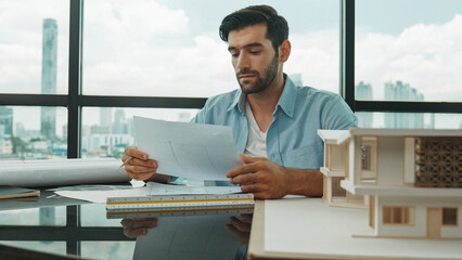 Skilled smart architect engineer writing house construction on blueprint at table with house model,...