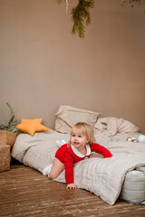 Cute baby toddler girl child in a red suit lies on the bed during the Christmas holiday at home.
