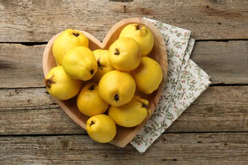 Tasty ripe quinces in heart shaped bowl on wooden table, top view