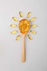 Wooden spoon with vitamin capsules on light background, top view