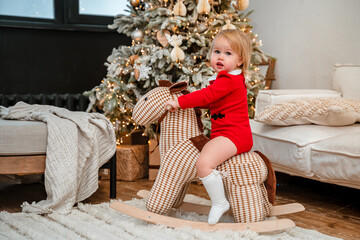 Cute baby child toddler rides a rocking horse in front of a Christmas tree, a pleasant atmosphere of New year and Christmas