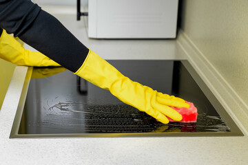 woman in rubber gloves washes the hob in the kitchen