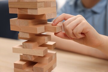 Child playing Jenga at wooden table indoors, closeup