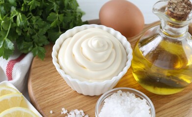 Fresh mayonnaise sauce in bowl and ingredients on table, closeup