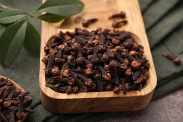 Wooden tray with aromatic cloves and green leaves on table, closeup