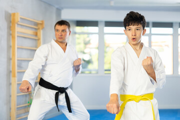 Adult man and boy teenager in kimono practice karate technique in gym
