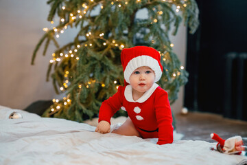 Obraz na płótnie Canvas Cute baby toddler girl child in a red suit and santa hat during the Christmas holiday at home. Selective focus. The concept of New year and Christmas, the atmosphere of fun and comfort.