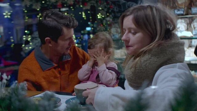 Family with toddler drinking hot chocolate and cocoa in the cafe after Christmas market. Leisure activity on holidays with family.