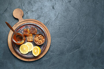 Board with jar of honey, lemon slices and nuts on dark background