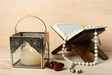 Muslim lamp with burning candle, dates, Koran and prayer beads on light wooden background