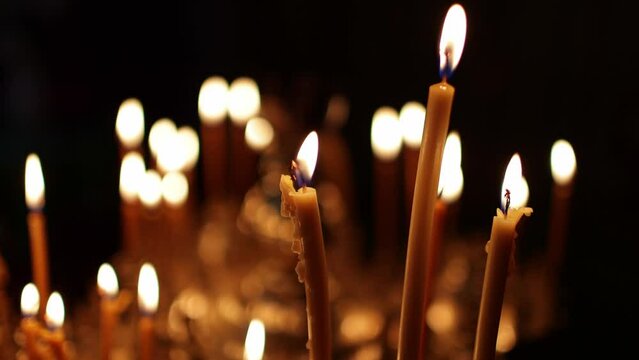 Close up burning candles in the Orthodox church. Memorial wax candles flicker with fire flame on large gold candlestick in the temple against dark. Concept of religion and faith in god