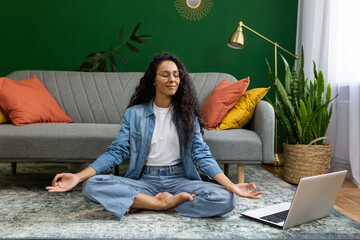 Young woman resting meditating in lotus pose sitting on floor at home in living room cinema,...