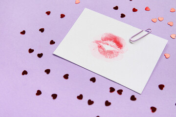 Paper with lipstick kiss mark and hearts on lilac background