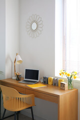 Comfortable workplace with modern laptop and narcissus flowers on table in room
