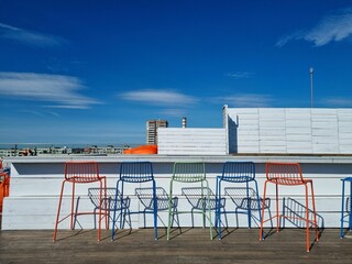 four colorful metal stools sit on a wooden deck with an umbrella