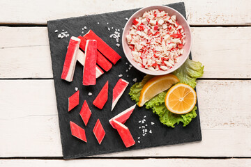 Slate board with tasty crab sticks on light wooden background © Pixel-Shot