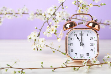 Blooming spring branches and alarm clock on white wooden table near purple wall