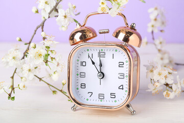 Blooming spring branches and alarm clock on white wooden table near purple wall